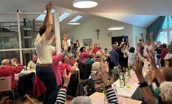 Viele sitzende und tanzende Personen in einem großen Raum.
