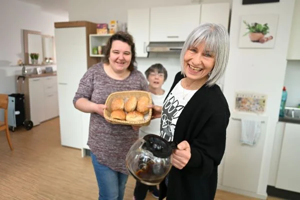 Das Bild zeigt drei Frauen die zusammen einen Brotkorb und eine Kaffeekanne halten