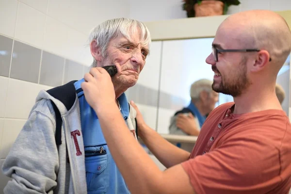 Das Bild zeigt einen Mann, der einen anderen rasiert