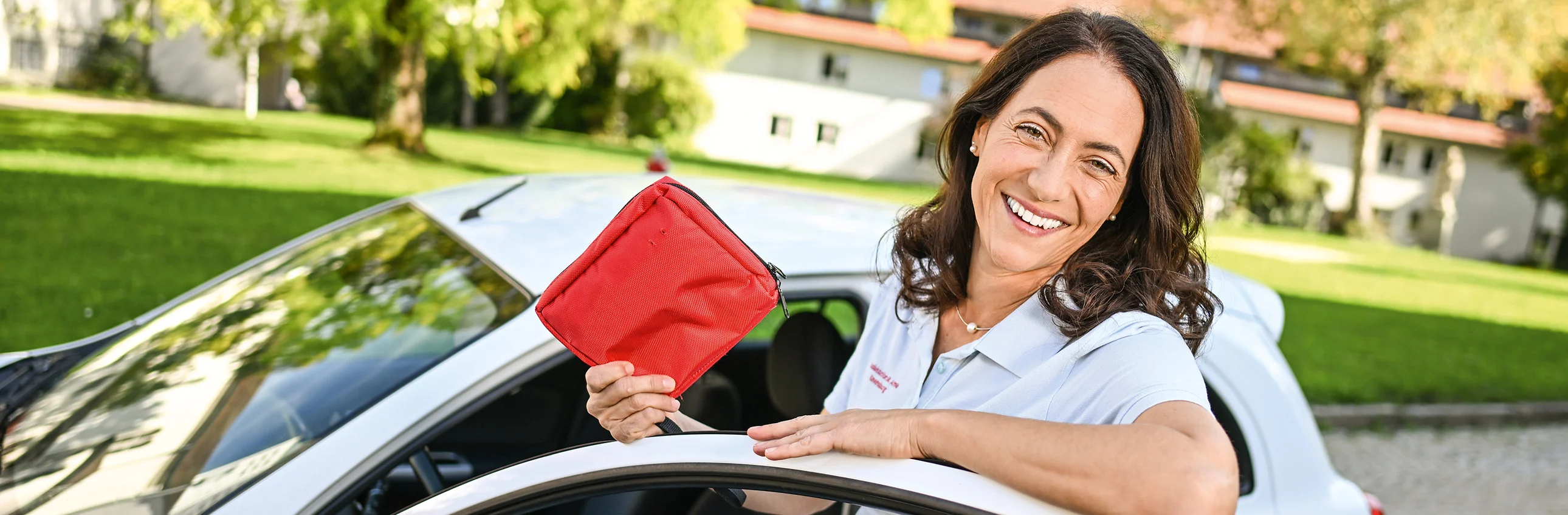 Das Bild zeigt eine Frau die ein Heft in der Hand hält und bei einem Auto steht