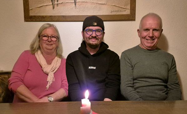 Drei Personen sitzen an einem Tisch und lächeln in die Kamera.