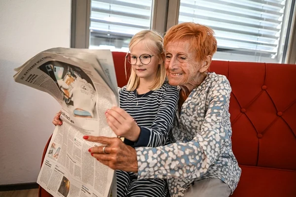 Das Bild zeigt eine Frau mit einem Kind beim Zeitunglesen
