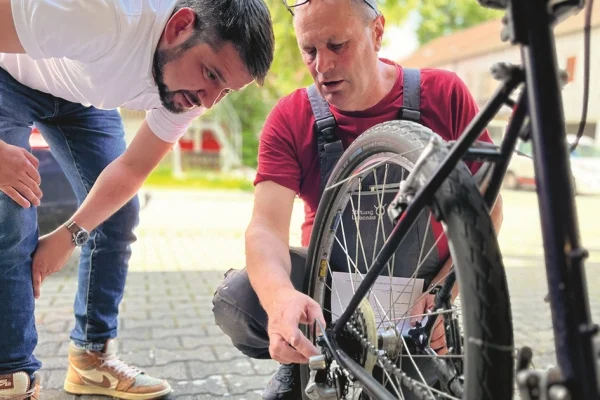 Das Bild zeigt zwei Männer, die an einem Fahrrad arbeiten Das Bild zeigt zwei Männer, die an einem Fahrrad arbeiten