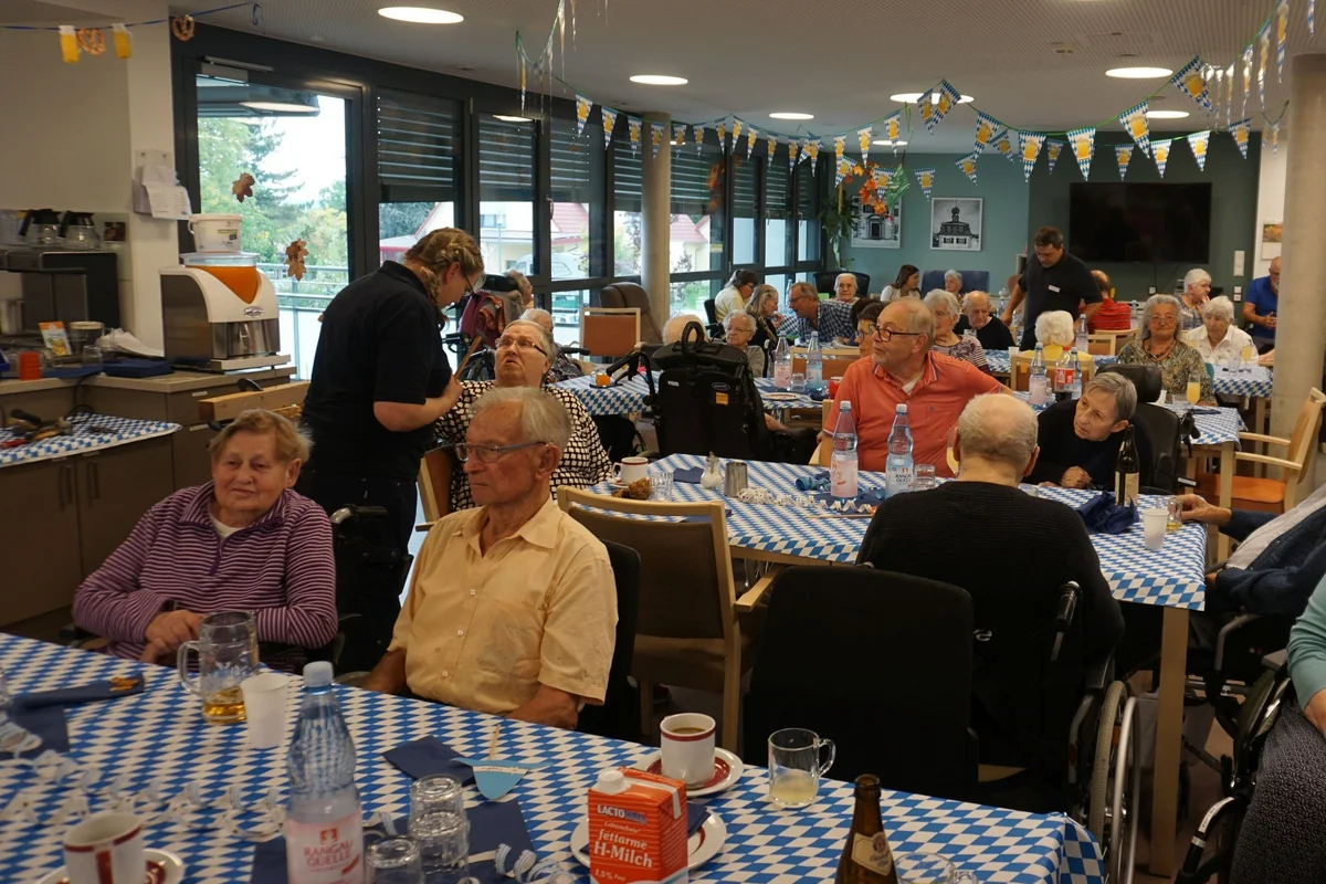 Stimmungsvolles Oktoberfest Gruppe älterer Menschen in festlich dekoriertem Gemeinschaftsraum, mehrere Tische mit blau-weiß karierten Tischdecken, Getränke und Gespräche.