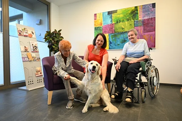 Das Bild zeigt drei Personen mit einem Hund im Eingagsbereich des OJK