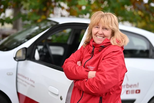 Das Bild zeigt eine Frau vor einem offenen Auto
