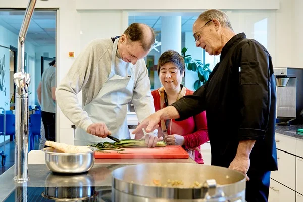 Das Bild zeigt drei Personen in einer Küche beim Kochen