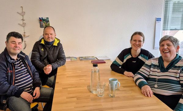 Vier Personen sitzen an einem Tisch und schauen in die Kamera.