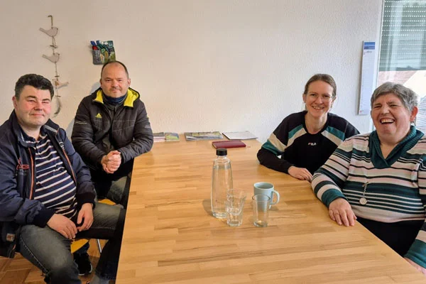 Vier Personen sitzen an einem Tisch und schauen in die Kamera.