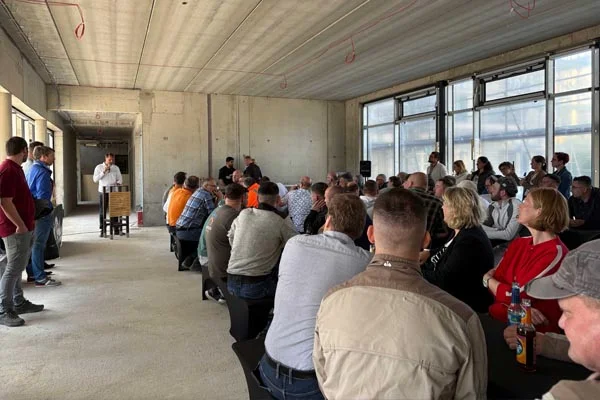 Richtfest Viele Personen sitzen auf Bänken und hören einer Person bei einer Rede zu.