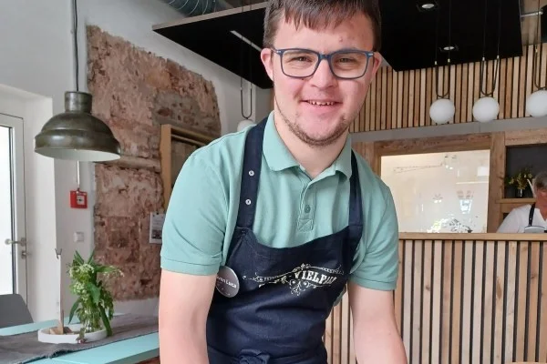 Begegnung im Café Vielfalt Das Bild zeigt einen jungen Mann mit Schürze in einem Cafe
