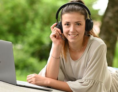 das bild zeigt eine junge frau mit kopfhörer liegend vor einem laptop