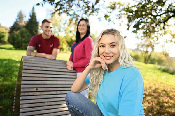 Unsere Mitarbeitende Das Bild zeigt drei Personen. Die Frau im Vordergrund trägt ein blaues Oberteil und lächelt in die Kamera
