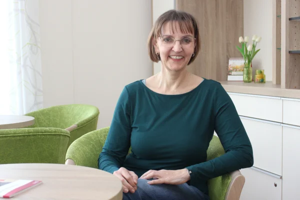 Eine Frau sitzt auf einem Stuhl und lächelt in die Kamera.