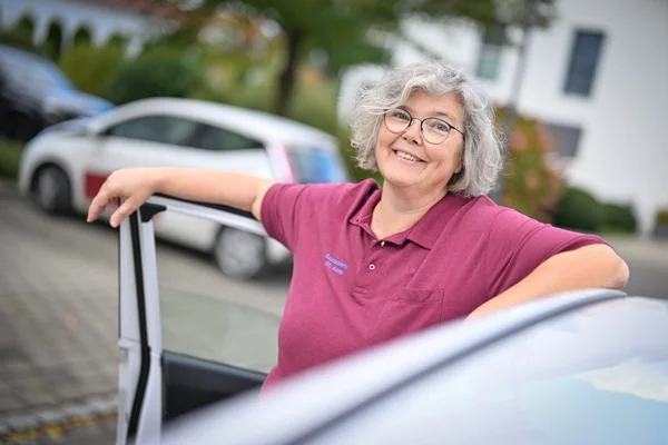 Das Bild zeigt eine Frau vor einer geöffneten Autotür