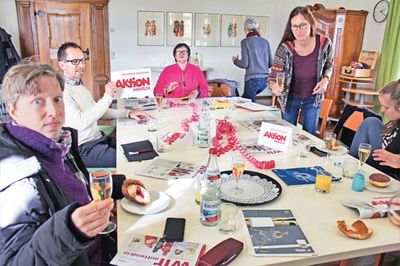 Redaktion Mehrere Personen sitzen an einem Tisch mit Schreibmaterial.