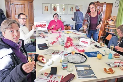 Redaktion Mehrere Personen sitzen an einem Tisch mit Schreibmaterial.