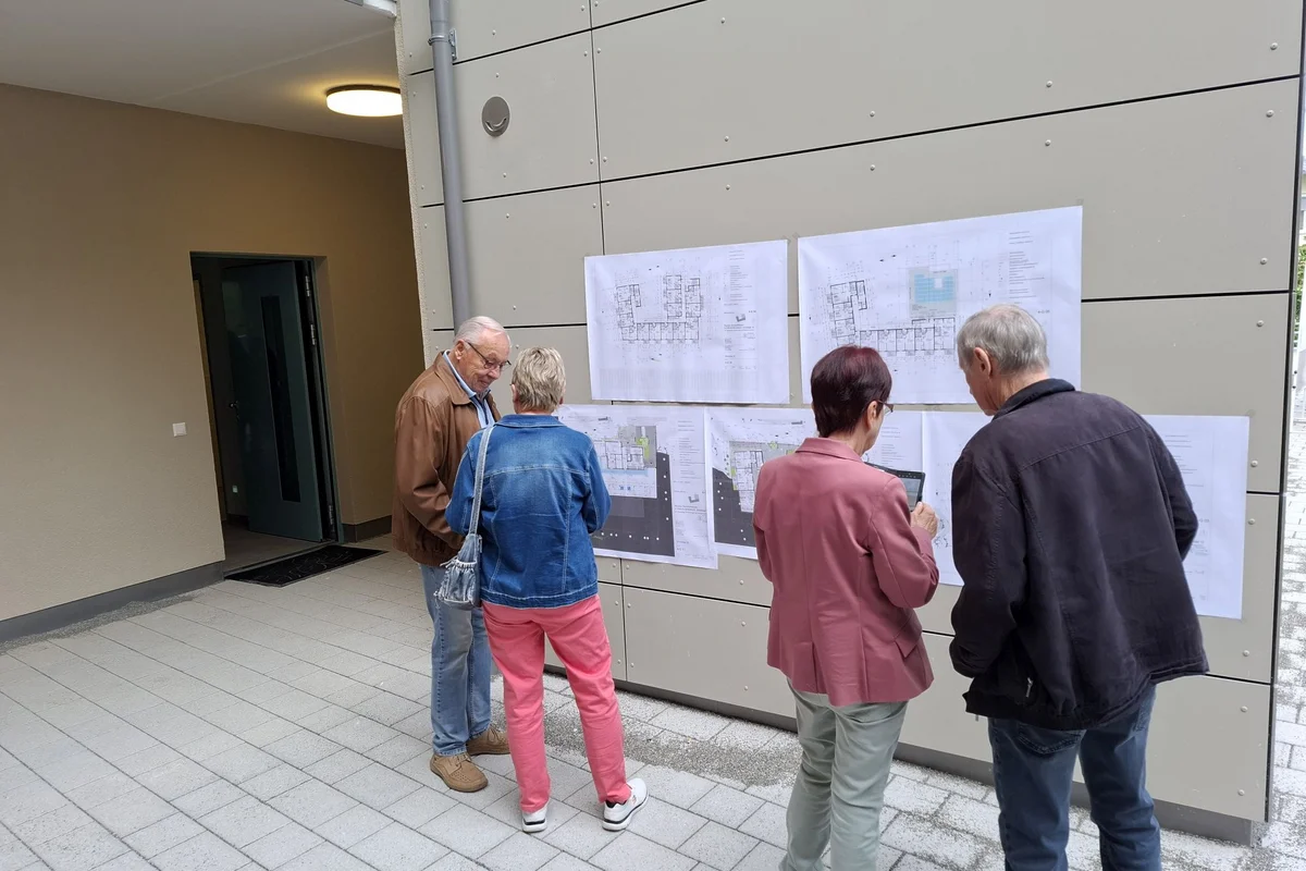 Tag der offenen Baustelle Vier Personen stehen in einem Gebäudegang und betrachten an der Wand ausgehängte Baupläne und Zeichnungen.