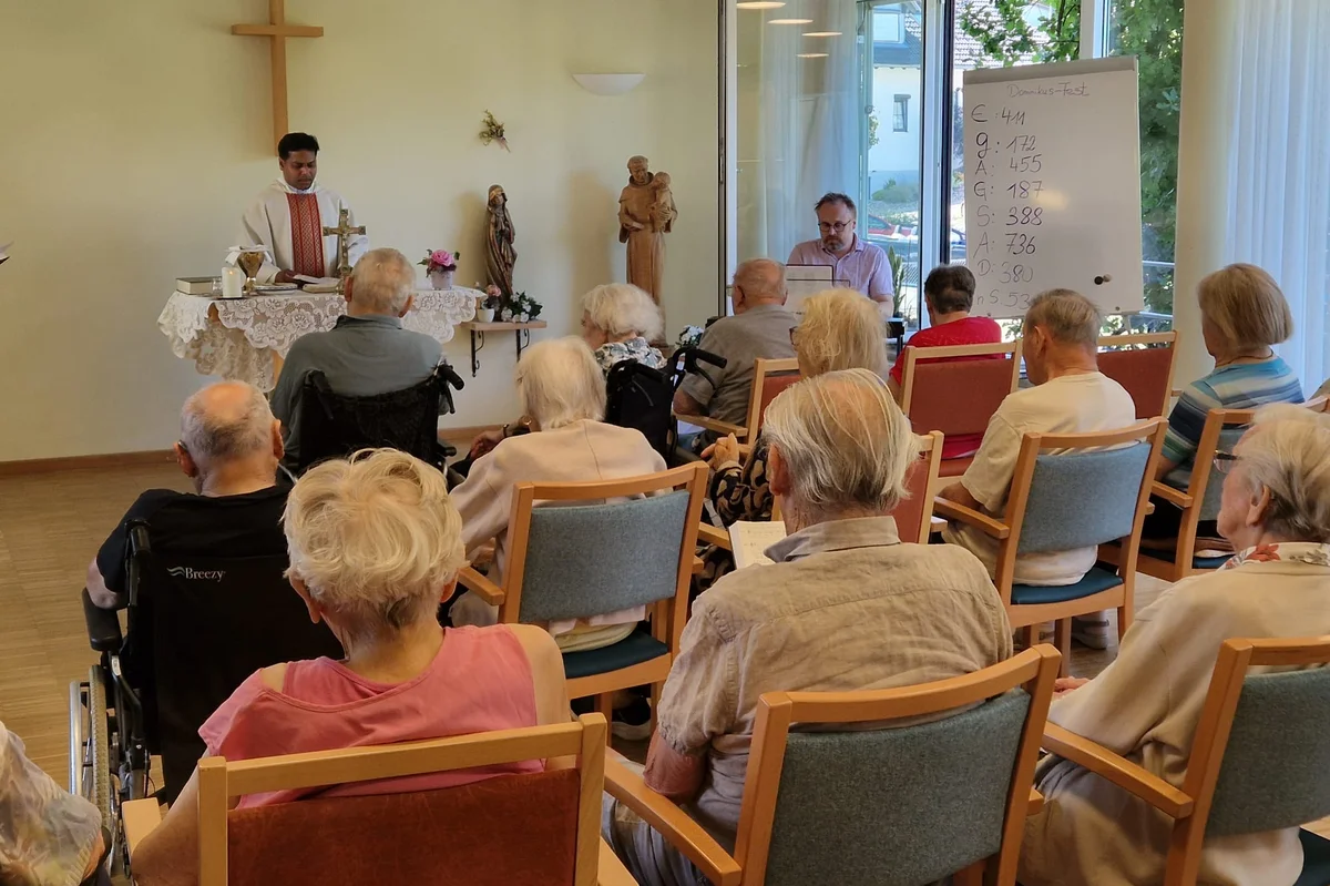 Patrozinium im Haus der Pflege St. Dominikus in Bad Grönenbach Mehrere Personen sitzen auf Stühlen und schauen zu einem Mann in einem Gewand der zu ihnen redet.