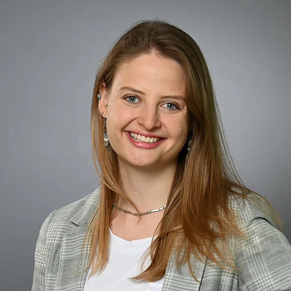 Meike Nowak Porträt einer lächelnden jungen Frau mit schulterlangen hellbraunen Haaren vor neutralem grauem Hintergrund
