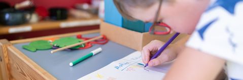 Das Bild zeigt ein malendes Kind an einem Tisch