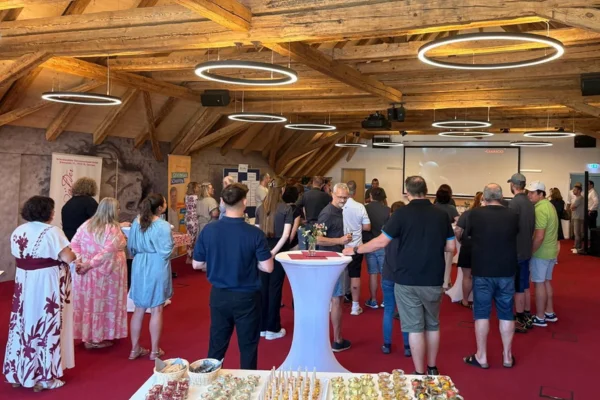 St. Georgen Viele Personen stehen in einem großen Raum und hören einem Vortrag zu.