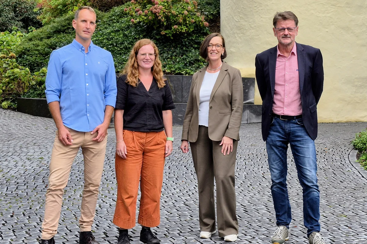 Neue Sozialdezernentin Petra Lill zu Antrittsbesuch in der Stiftung Liebenau Vier Erwachsene — zwei Männer und zwei Frauen — stehen nebeneinander auf einem Kopfsteinpflasterweg vor dem schloss Liebenau, in lässig-formeller Kleidung in die Kamera blickend.