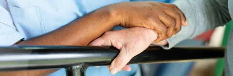 Eine Hand stützt eine andere Hand beim Gehen an einem Geländer.