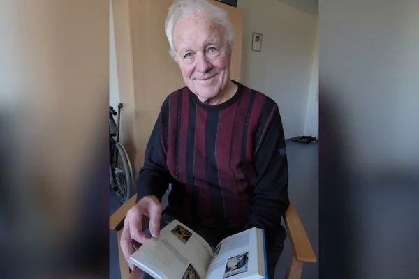 Das Bild zeigt einen Mann mit grauen Haaren und einem gestreiften Pullover, der gerade ein Buch liest