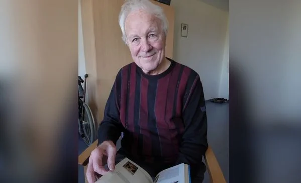 Das Bild zeigt einen Mann mit grauen Haaren und einem gestreiften Pullover, der gerade ein Buch liest