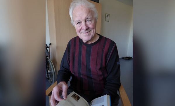 Das Bild zeigt einen Mann mit grauen Haaren und einem gestreiften Pullover, der gerade ein Buch liest