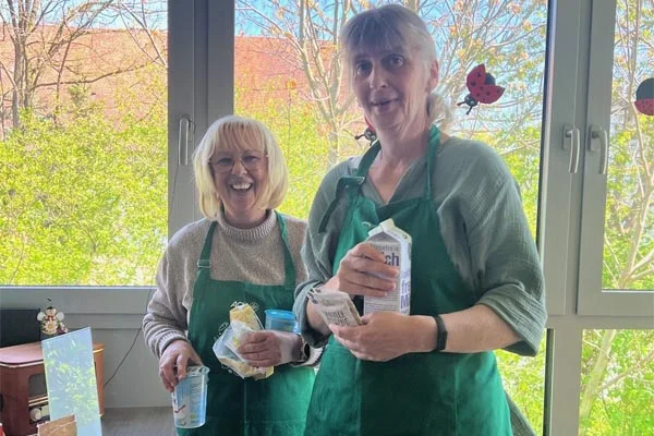 AOK-Workshop Zwei Frauen mit Kochschürzen halten Zutaten in der Hand.