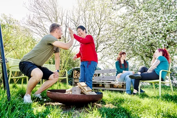 Das Bild zeigt mehrere Personen im Garten spielend und sich unterhaltend