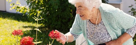 Das Bild zeigt eine ältere Frau im Garten mit einer Blume