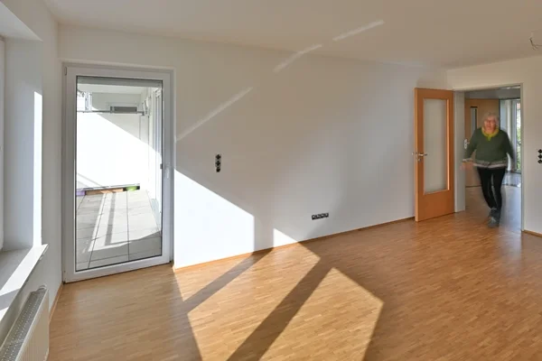 Wohnanlage Berg Das Bild zeigt eine Person in einem Zimmer mit Balkon in einer leeren Wohnung