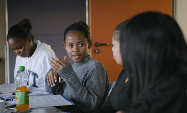 Mehrere Personen sitzen an einem Tisch und eine Frau spricht.