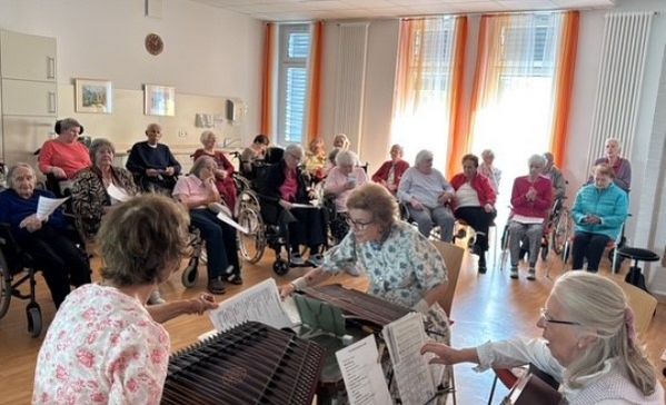 Das Bild zeigt drei Musizierende mit Zuhörern