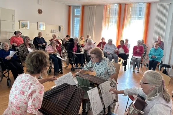 Das Bild zeigt drei Musizierende mit Zuhörern