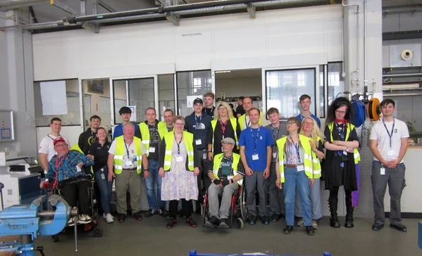 Tandem-Projekt von der Stiftung Liebenau und Rolls Royce Power Systems Gruppenbild verschiedener Personen in Warnwesten in einem Gebäude.