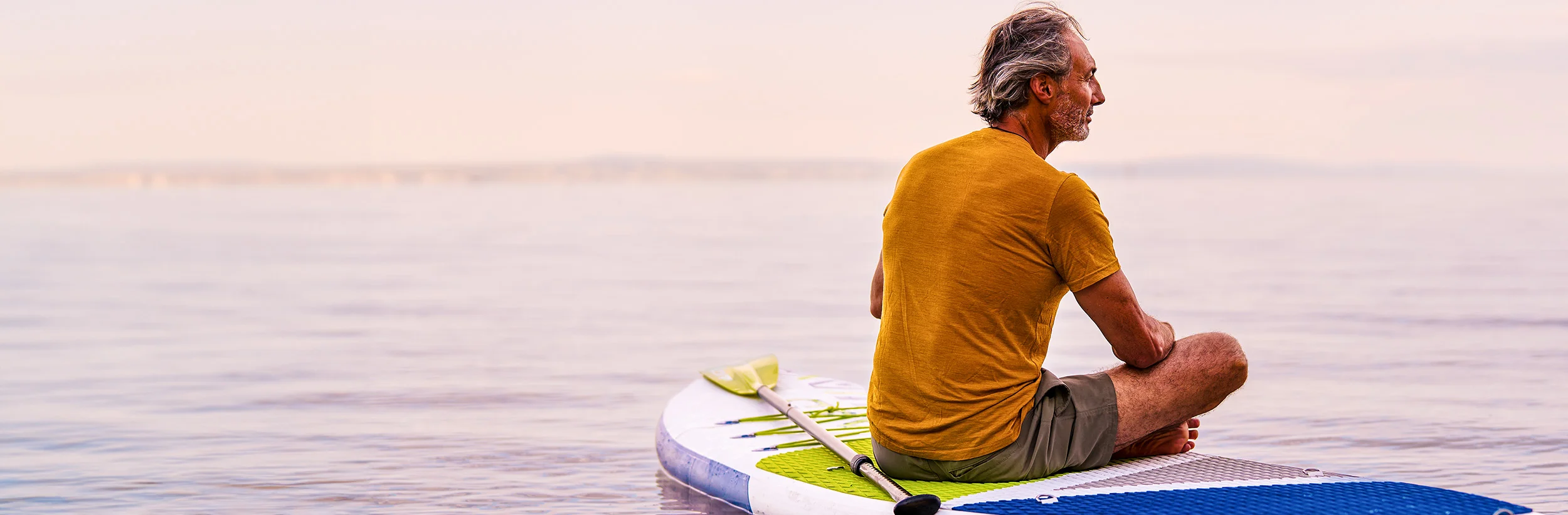 Ein Mann der auf einem Stand Up Paddle Board auf einem See sitzt und in die Ferne schaut.