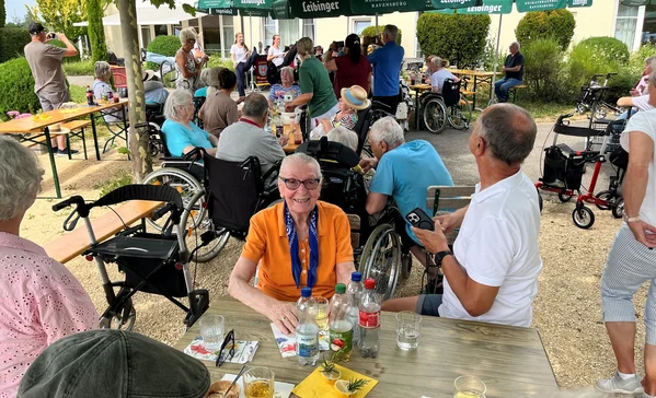 Viele Personen bei einem Sommerfest sitzen unter Schirmen.