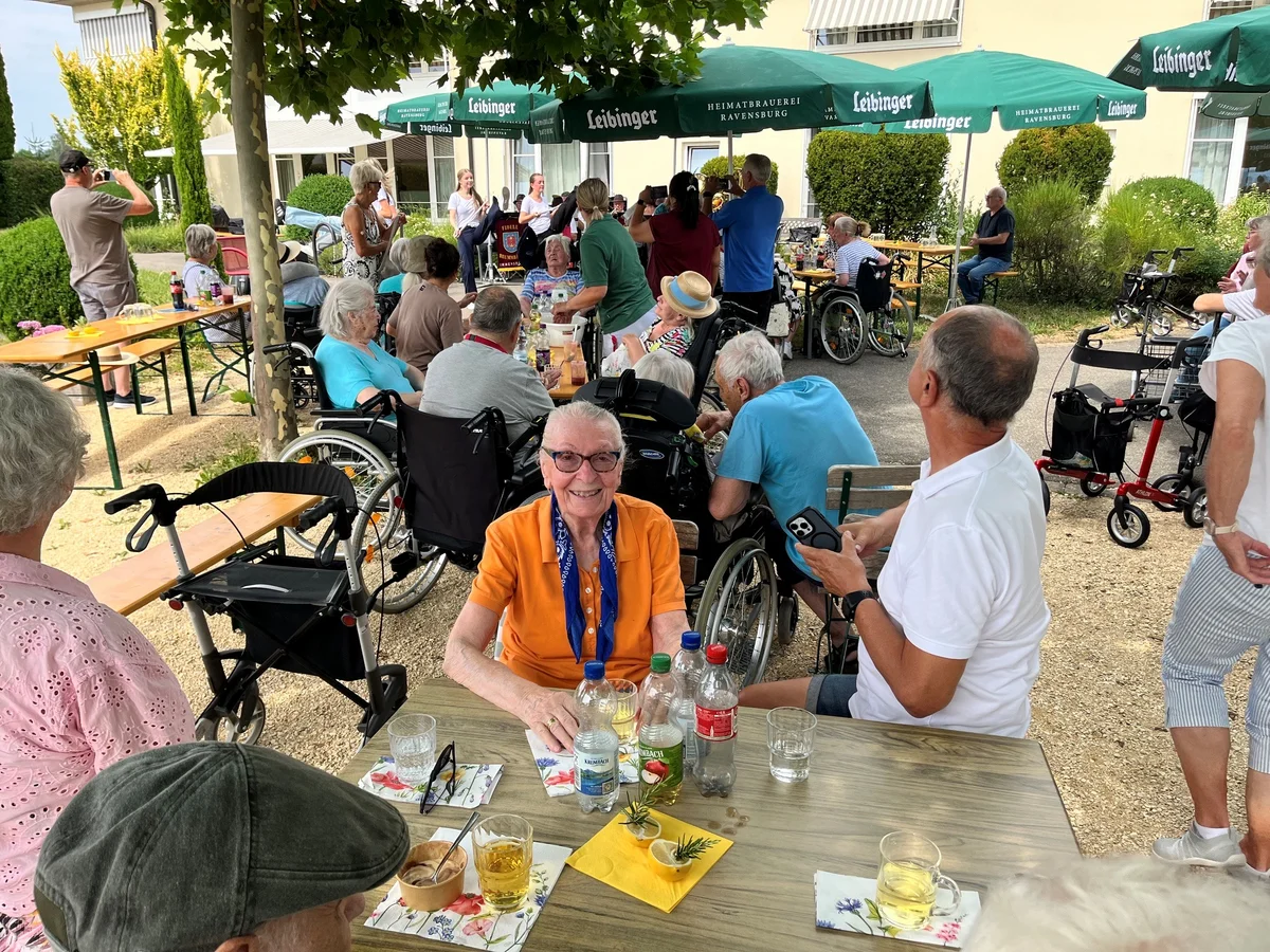 Viele Personen bei einem Sommerfest sitzen unter Schirmen.