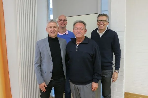 Das Bild zeigt vier Männer die im Anzug vor der Kamera stehen und lächeln