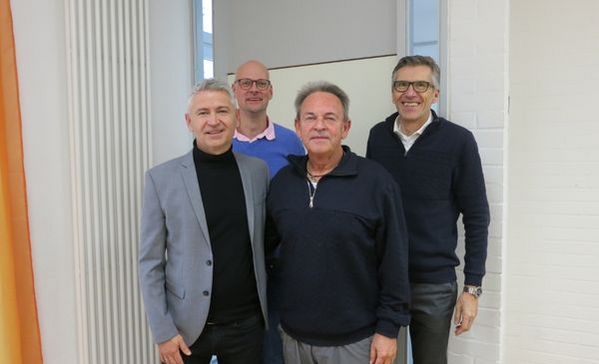 Das Bild zeigt vier Männer die im Anzug vor der Kamera stehen und lächeln