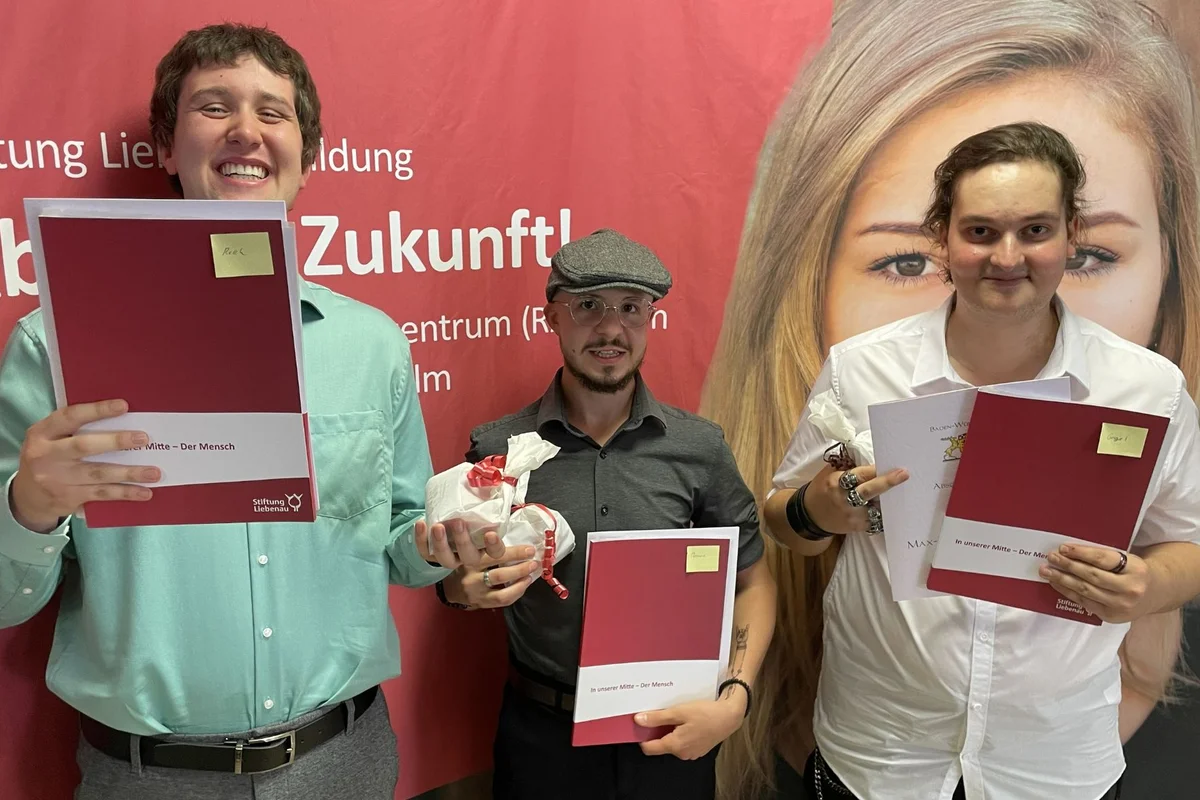Absolventenfeier Drei Männer halten lächelnd ihre Zeugnismappen vor sich und schauen in die Kamera.