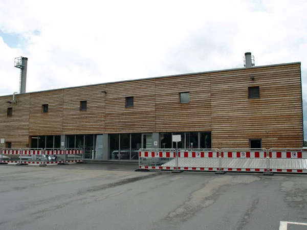 Die neue Energiezentrale in Liebenau Das Bild zeigt ein großes steinernes Gebäude und einen großen Parkplatz