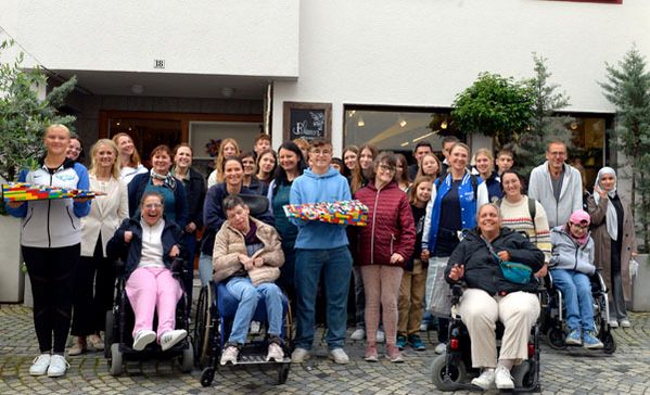 das bild zeigt eine große gruppe menschen mit und ohne behinderung, teilweise in rollstühlen, die bauteile der lego-rampe in der hand halten