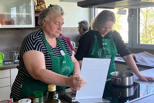 AOK-Workshop Zwei Frauen beim Kochen mit Rezept in der Hand.