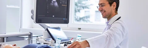 Das Bild zeigt einen Arzt mit einem liegenden Patienten bei der Sonographie