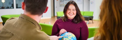 Das Bild zeigt eine junge Frau mit einer Weltkugel in der Handmit zwei weiteren Personen